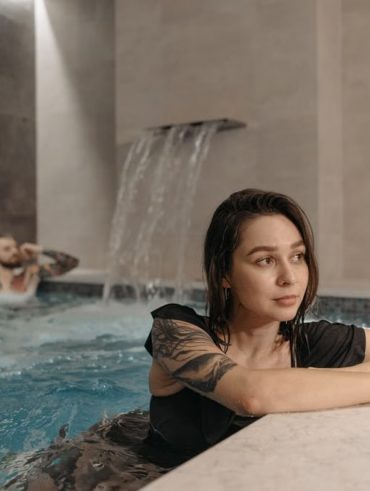 Tattooed woman and man enjoying a modern indoor pool setting, emphasizing relaxation.