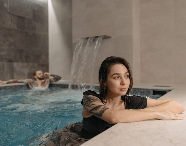 Tattooed woman and man enjoying a modern indoor pool setting, emphasizing relaxation.