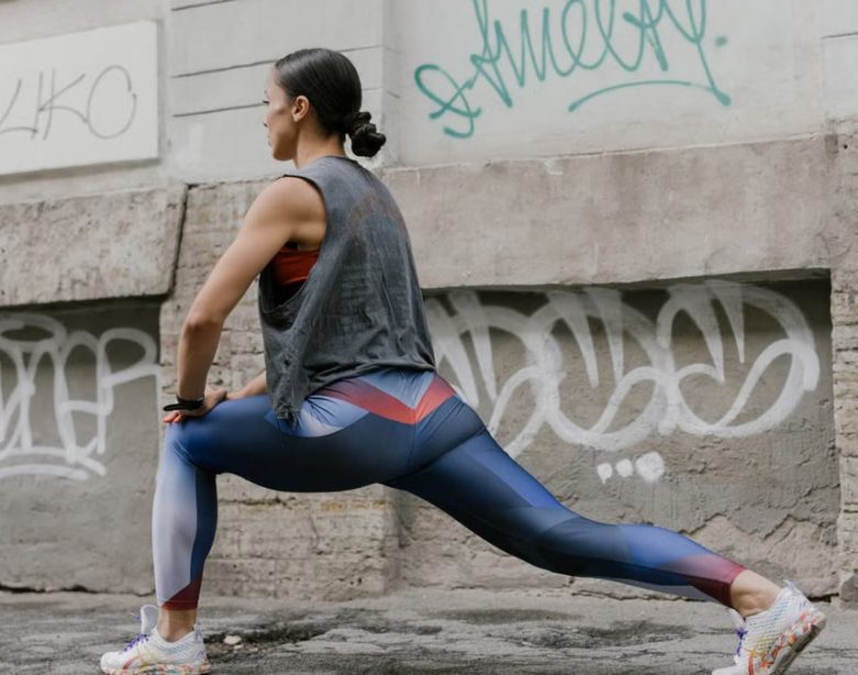 Woman doing lunges for fitness against an urban graffiti wall, showcasing exercise and wellness.