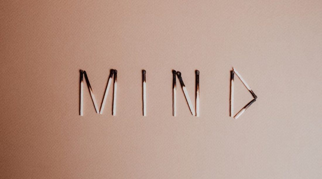 Creative still life of burnt matchsticks spelling 'Mind' on a textured beige surface.