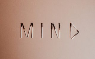 Creative still life of burnt matchsticks spelling 'Mind' on a textured beige surface.