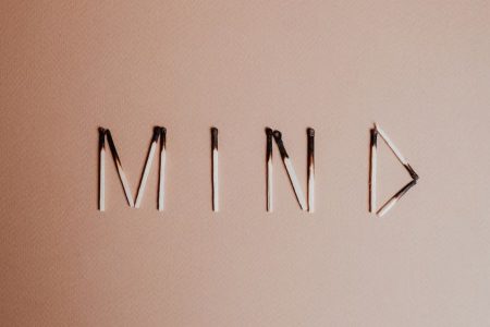 Creative still life of burnt matchsticks spelling 'Mind' on a textured beige surface.