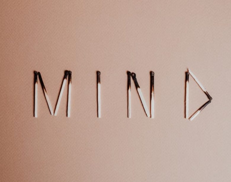 Creative still life of burnt matchsticks spelling 'Mind' on a textured beige surface.